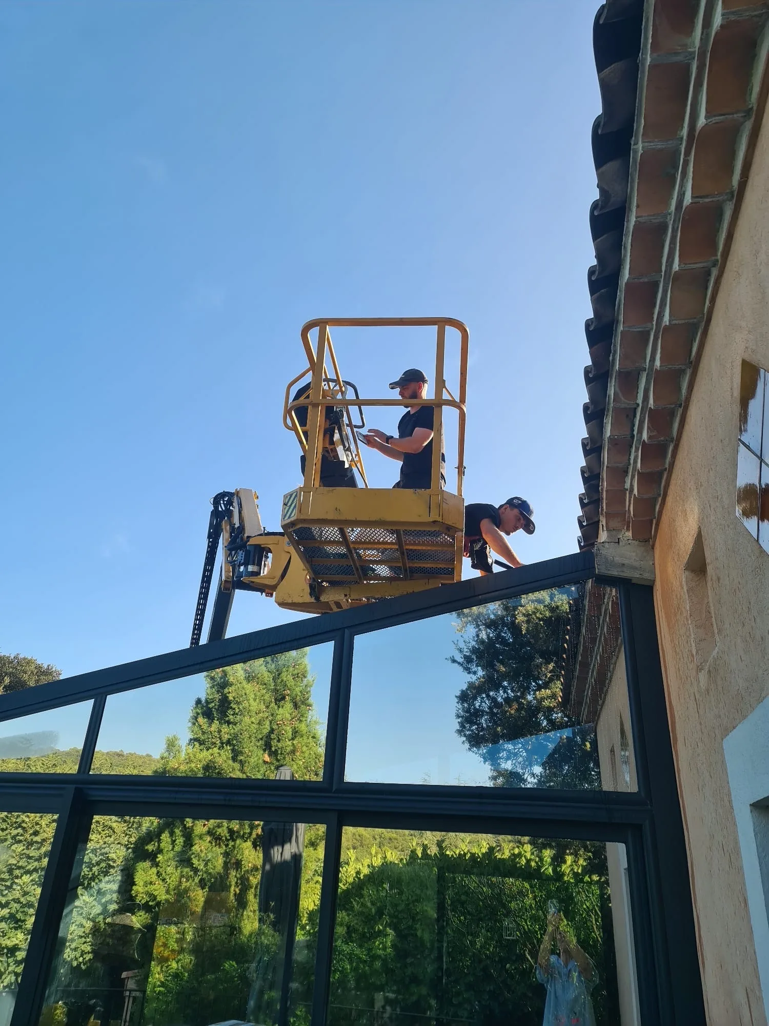 Vue depuis le panier de la nacelle sur une véranda vitrée et le jardin d'une bastide varoise